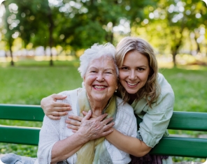 Woman holding a lady who is sitting on a bench